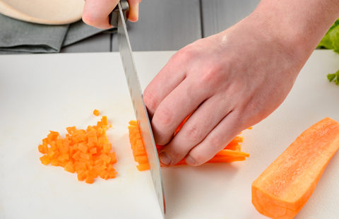 Chef chopping carrot sticks into a small dice, closeup shot. Man performing good knife skills during cooking a meal.